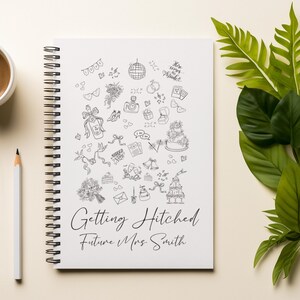 May include: A spiral-bound notebook with a white cover featuring black line art of wedding-related icons. The text "Getting Hitched Future Mrs. Smith" is written in elegant script. A cup of coffee, a pencil, and green leaves are also in the image.