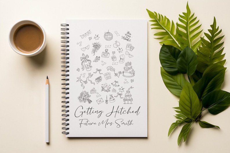 May include: A spiral-bound notebook with a white cover featuring black line art of wedding-related icons. The text "Getting Hitched Future Mrs. Smith" is written in elegant script. A cup of coffee, a pencil, and green leaves are also in the image.