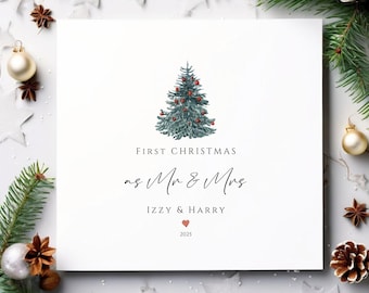 May include: A white card with a watercolor illustration of a Christmas tree decorated with red ornaments. The text reads "First Christmas as Mr & Mrs" with the names "Izzy & Harry" and the year "2025".