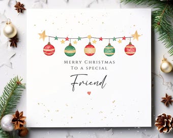 May include: A white Christmas card with the message "Merry Christmas to a special Friend." The card features a string of ornaments and stars in red, green, and gold. A small red heart is below the word "Friend."