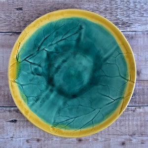 May include: A round ceramic plate with a green centre and a yellow rim. The plate has a leaf design.