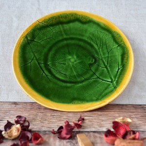 May include: A green ceramic plate with a yellow rim and a leaf design. The plate is on a wooden surface.