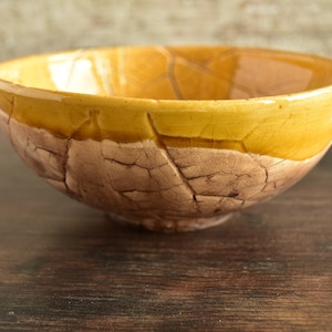 May include: A yellow and brown ceramic bowl with a textured, leaf-like design. The bowl is glazed and has a glossy finish.