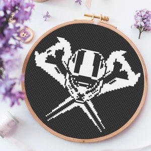 May include: A black and white cross-stitch embroidery hoop with a pixelated image of a robot wearing headphones. The robot has a large head and two arms that are crossed in front of it.