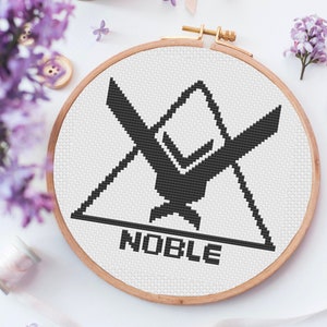 May include: A black and white cross stitch pattern of a symbol with the word "NOBLE" underneath. The pattern is framed in a wooden hoop.