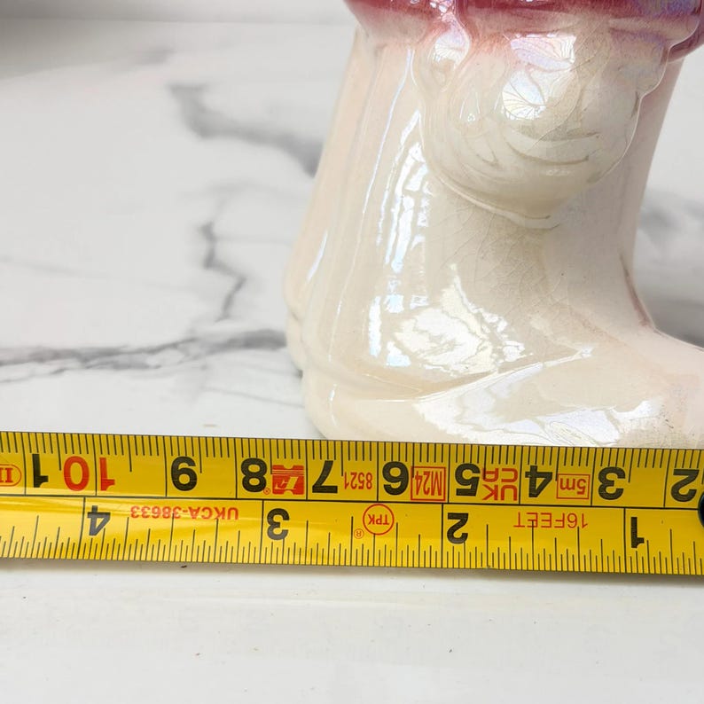 Close-up of a measuring tape with markings in inches and centimeters laid across a white marble surface, with the base of a ceramic figurine visible.