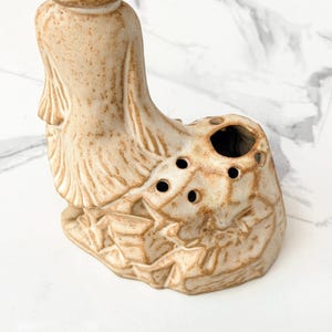 Close-up of a vintage ceramic incense holder shaped like a seated figure with multiple holes for incense sticks.