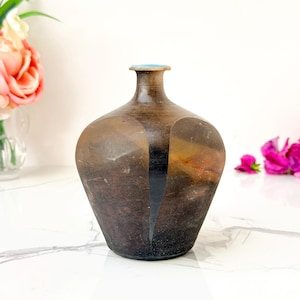 May include: A small, rounded ceramic vase with a narrow neck and a flat, turquoise-coloured rim. The body features a dark, mottled brown and black finish with a distinct, smooth, vertical black stripe running down the centre of the front surface.