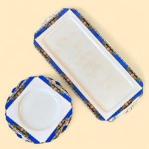 May include: Two-piece set of vintage serving dishes. The set includes a rectangular tray and a square plate. Both pieces have a white base with a blue border and floral accents. The edges are scalloped.