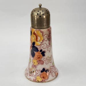 May include: A vintage salt shaker with a floral design. The ceramic base features a pattern of yellow, orange, and blue flowers on a cream background. The top is made of metal with small holes for dispensing.