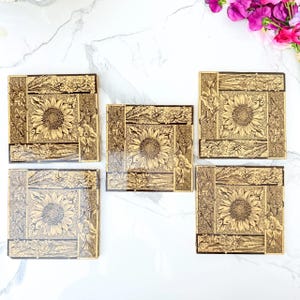 May include: A set of five square coasters featuring a gold and black sunflower design. Each coaster displays a central sunflower surrounded by floral borders and a textured, crackled background pattern, creating a cohesive botanical aesthetic.