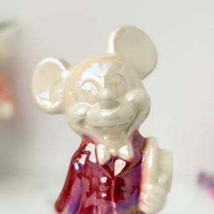 A pearlescent ceramic figurine of Mickey Mouse in a maroon suit and bowtie, with a slight sheen and soft lighting.