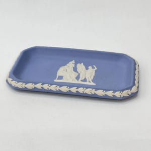 May include: A rectangular blue ceramic tray with a white leaf pattern around the edges. The tray features a white relief design of classical figures. A decorative piece for the home.