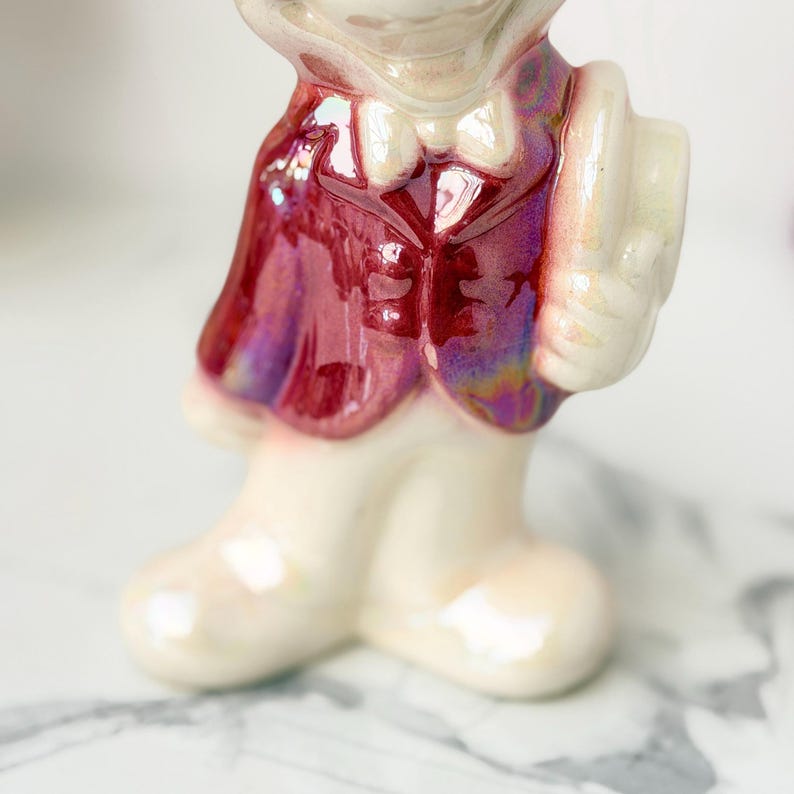 Close-up of a ceramic figurine's lower body, featuring a white, pearlescent base and legs, with a glossy, iridescent burgundy jacket.