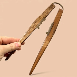 Puede incluir: Un cascanueces vintage de madera y metal. Los mangos de madera son de color marrón cálido y los dientes de metal son plateados. El cascanueces tiene un diseño sencillo y clásico, con un anillo de metal en la parte superior.