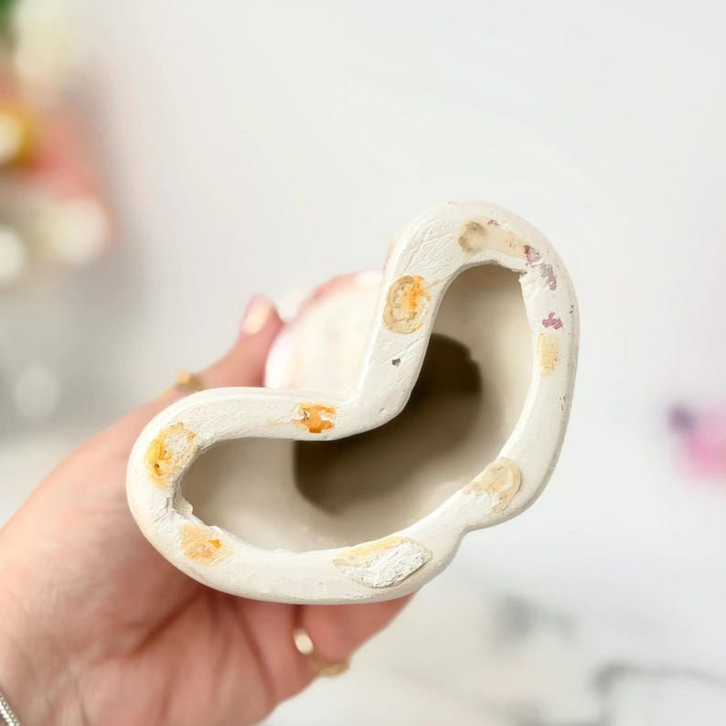 Close-up of a hand holding a white ceramic curved sculpture with chipped pastel paint patches.