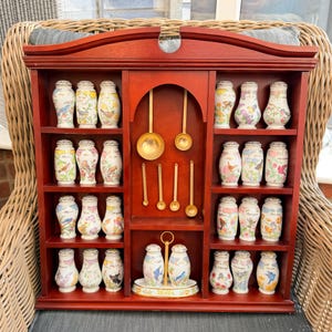 Peut inclure: Une étagère à épices en bois avec une finition cerisier foncé, comprenant trois étagères de chaque côté contenant vingt-quatre pots à épices en porcelaine ornés d'illustrations d'oiseaux et de fleurs, et six cuillères en métal doré au centre.
