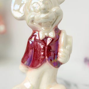 Close-up of a pearlescent ceramic mouse figurine wearing a deep red vest and a white bow tie, with a subtle iridescent sheen.