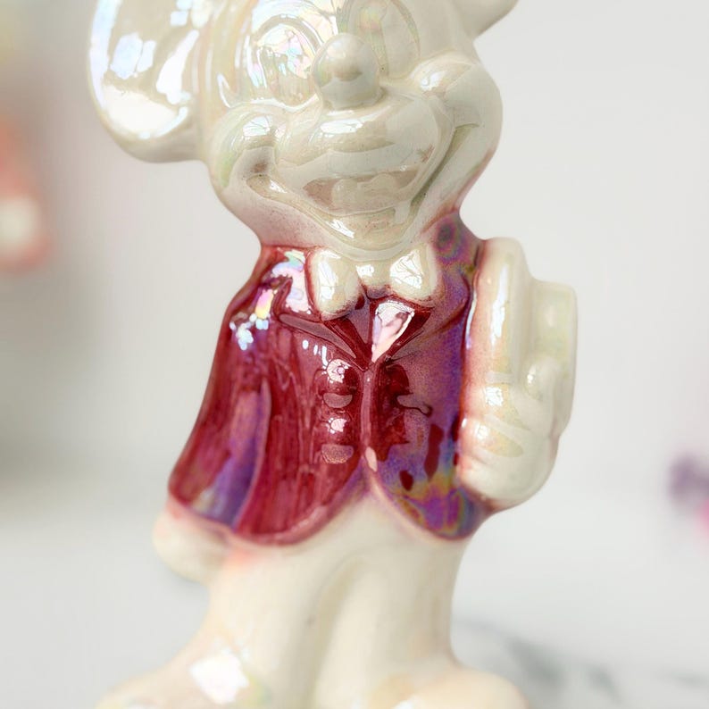 Close-up of a pearlescent ceramic mouse figurine wearing a deep red vest and a white bow tie, with a subtle iridescent sheen.