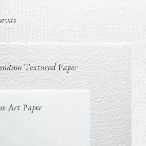 May include: Close-up of three different surfaces: canvas, premium textured paper, and fine art paper. The surfaces are white and have a subtle texture.
