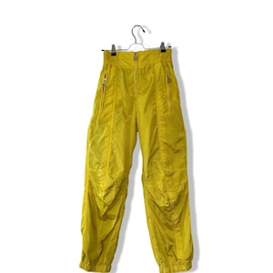 Może przedstawiać: Żółte spodnie z zamkiem błyskawicznym i wieloma kieszeniami. Spodnie mają sznurek w pasie i luźny krój.