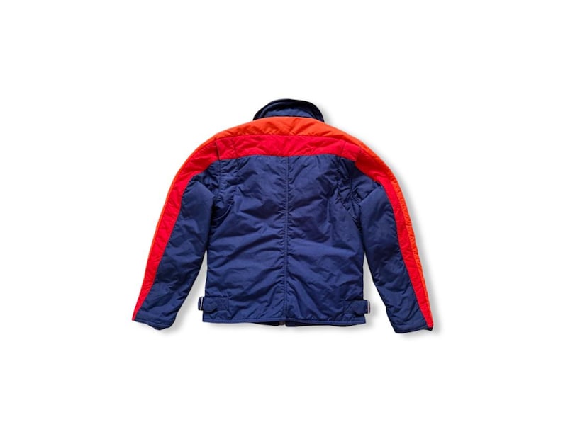 May include: A blue, red, and orange jacket. The jacket has a blue body with red stripes down the sleeves and across the shoulders. The collar is orange. The jacket has two small buckles at the waist.