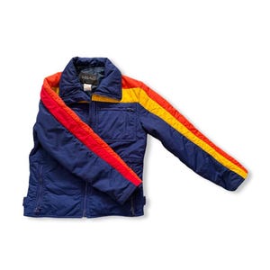 May include: A vintage blue jacket with red and yellow stripes on the sleeves and collar. The jacket has a zipper closure and a small pocket on the chest. The brand name "HEAD" is visible on the collar.
