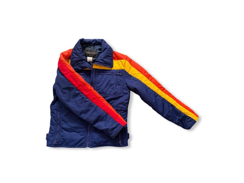 May include: A vintage blue jacket with red and yellow stripes on the sleeves and collar. The jacket has a zipper closure and a small pocket on the chest. The brand name "HEAD" is visible on the collar.