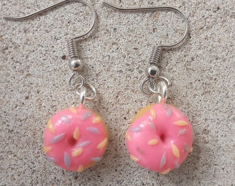 May include: A pair of pink donut earrings with silver hooks. The donuts are decorated with purple and yellow sprinkles.