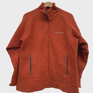 May include: Rust-colored fleece jacket with a full-length zipper and two side pockets. The jacket has a high collar and the brand name "mont bell" is embroidered on the chest. The jacket is hanging on a wooden hanger.