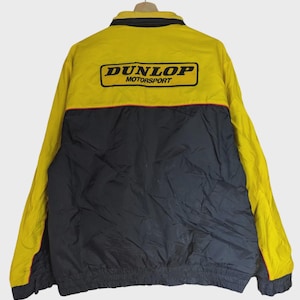May include: Yellow and black Dunlop Motorsport jacket. The jacket features a yellow upper section with the Dunlop Motorsport logo in black and white. The lower section is black, with a red stripe separating the two colors. The jacket has a collar and a zipper.