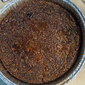 May include: A close-up of a brown, baked dessert in a silver aluminum pan. The dessert has a smooth, glossy top and a slightly crumbly texture.