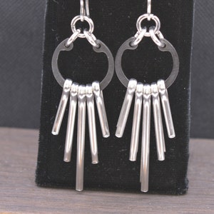 May include: A pair of silver earrings with a circle design and multiple dangling rods.