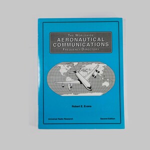 May include: A blue book titled "The Worldwide Aeronautical Communications Frequency Directory." The cover features a silver rectangle with the title, a world map, and an illustration of an airplane. The author's name is Robert E. Evans.