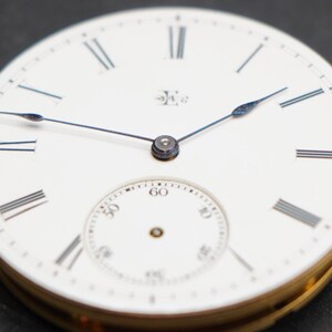 May include: A white pocket watch with Roman numeral hour markers and a smaller subdial. The watch hands are blue steel.