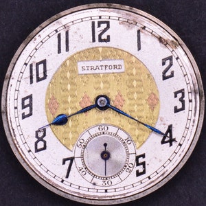 Pu&ograve; includere: Un orologio da tasca argentato con un quadrante bianco e indici orari romani neri. L'orologio ha un quadrante interno color oro con un motivo a rombi e la scritta "STRATFORD" stampata su di esso. L'orologio ha lancette blu.