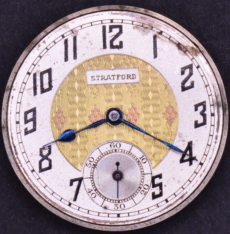 Pu&ograve; includere: Un orologio da tasca argentato con un quadrante bianco e indici orari romani neri. L'orologio ha un quadrante interno color oro con un motivo a rombi e la scritta "STRATFORD" stampata su di esso. L'orologio ha lancette blu.
