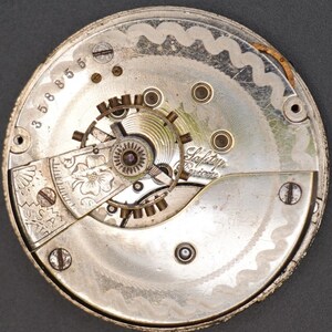 May include: Close-up of a silver pocket watch movement with the inscription "Safety Pinion" and the number "35885".