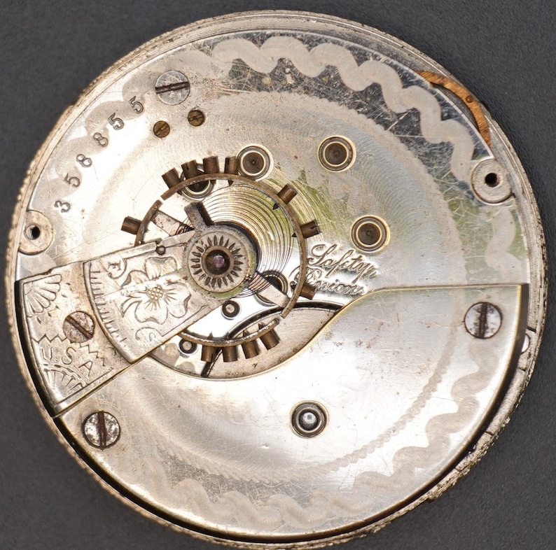 May include: Close-up of a silver pocket watch movement with the inscription "Safety Pinion" and the number "35885".