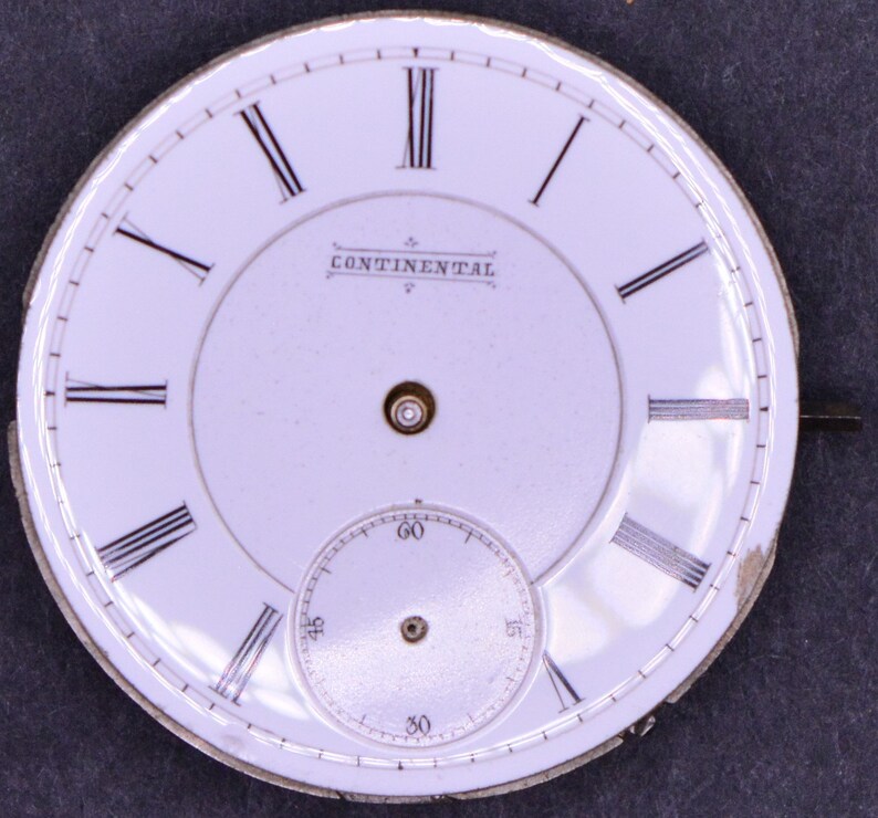 May include: White watch face with black Roman numeral hour markers and black minute markers. The watch face has the word "CONTINENTAL" printed in black.
