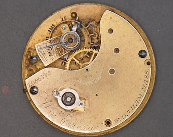 Op de afbeelding: Close-up van het binnenwerk van een goudkleurig zakhorloge met de inscriptie "Wm. Ellery" en "WALTHAM, MASS." Het horloge heeft serienummer "1,086332".