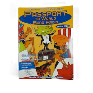 May include: A yellow and orange book cover with the title "Passport to World Band Radio" and the subtitle "Edition 2003". The cover features a cartoon illustration of a green alien conductor leading a band of musical instruments, including a trumpet, a tuba, a harp, and a violin. The book is described as "World's #1 Selling Shortwave Guide!"