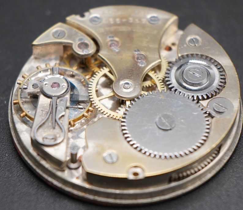May include: Close-up of a complex, intricate watch mechanism with gears and springs. The watch face is not visible, but the intricate workings of the movement are on display.