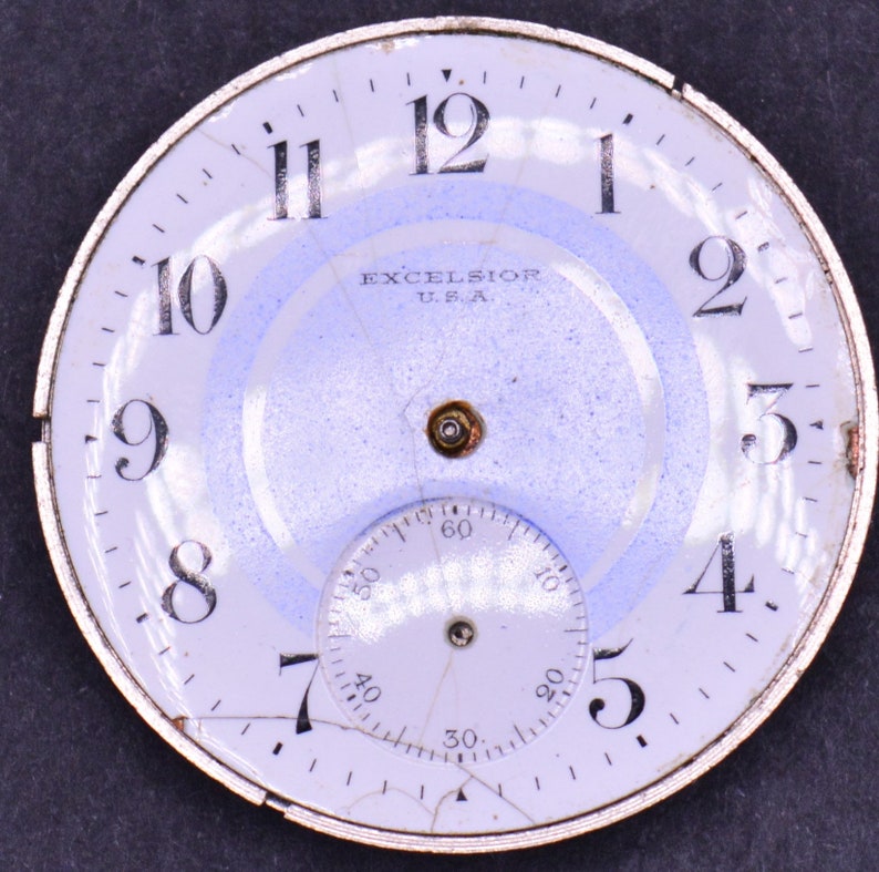 May include: White watch face with black numbers 1 through 12 and black markings for the minutes. The watch face also has a smaller white circle with black markings for the seconds. The watch face has the text "EXCELSIOR U.S.A." printed on it.