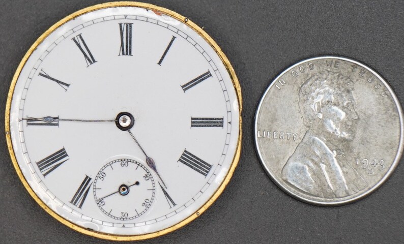 以下が含まれることがあります： ローマ数字の文字盤と金色の縁取りが付いた、ヴィンテージの懐中時計の文字盤のクローズアップ。時計の文字盤は、日本の1円玉と同じくらいの大きさです。