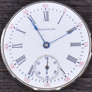 May include: A white pocket watch with Roman numeral hour markers and black hands. The watch face has the word "WALTHAM" printed on it. The watch has a smaller, circular sub-dial with black hands and Arabic numeral markers.