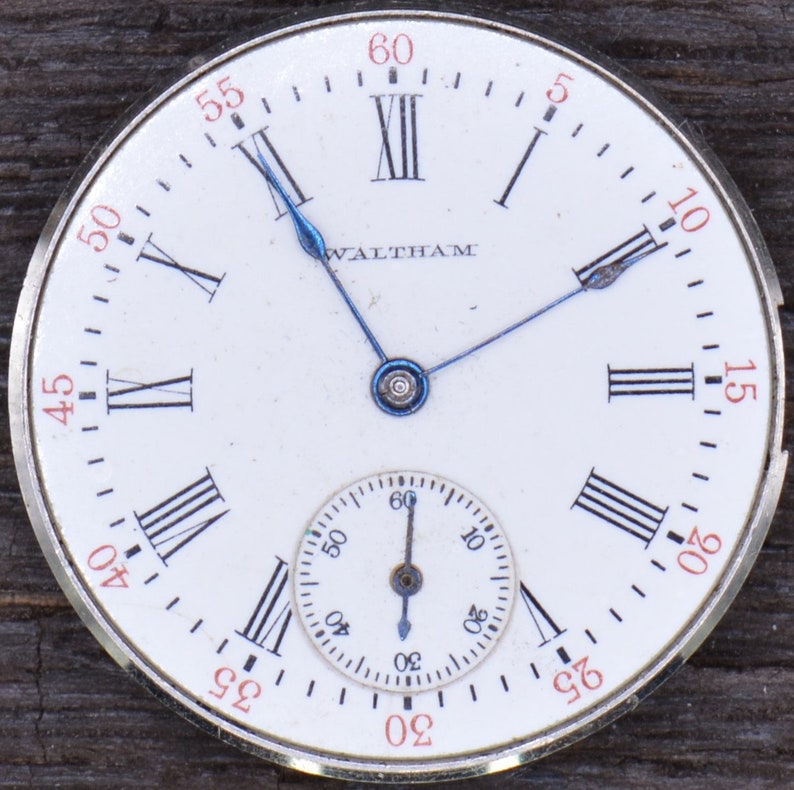 May include: A white pocket watch with Roman numeral hour markers and black hands. The watch face has the word "WALTHAM" printed on it. The watch has a smaller, circular sub-dial with black hands and Arabic numeral markers.