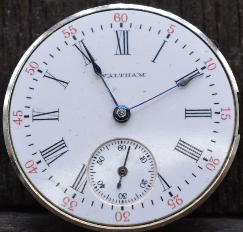 May include: A white pocket watch with Roman numeral markings and a smaller sub-dial. The watch face says "Waltham" and has black hands.