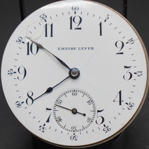 May include: A white pocket watch face with black Roman numeral hour markers and black hands. The watch face has a small sub-dial at the bottom and the text "EMPIRE LEVER" printed in black.