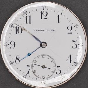May include: A white pocket watch face with black Roman numeral hour markers and black Arabic numeral minute markers. The watch face has a small seconds dial at the bottom. The watch face says "EMPIRE LEVER".